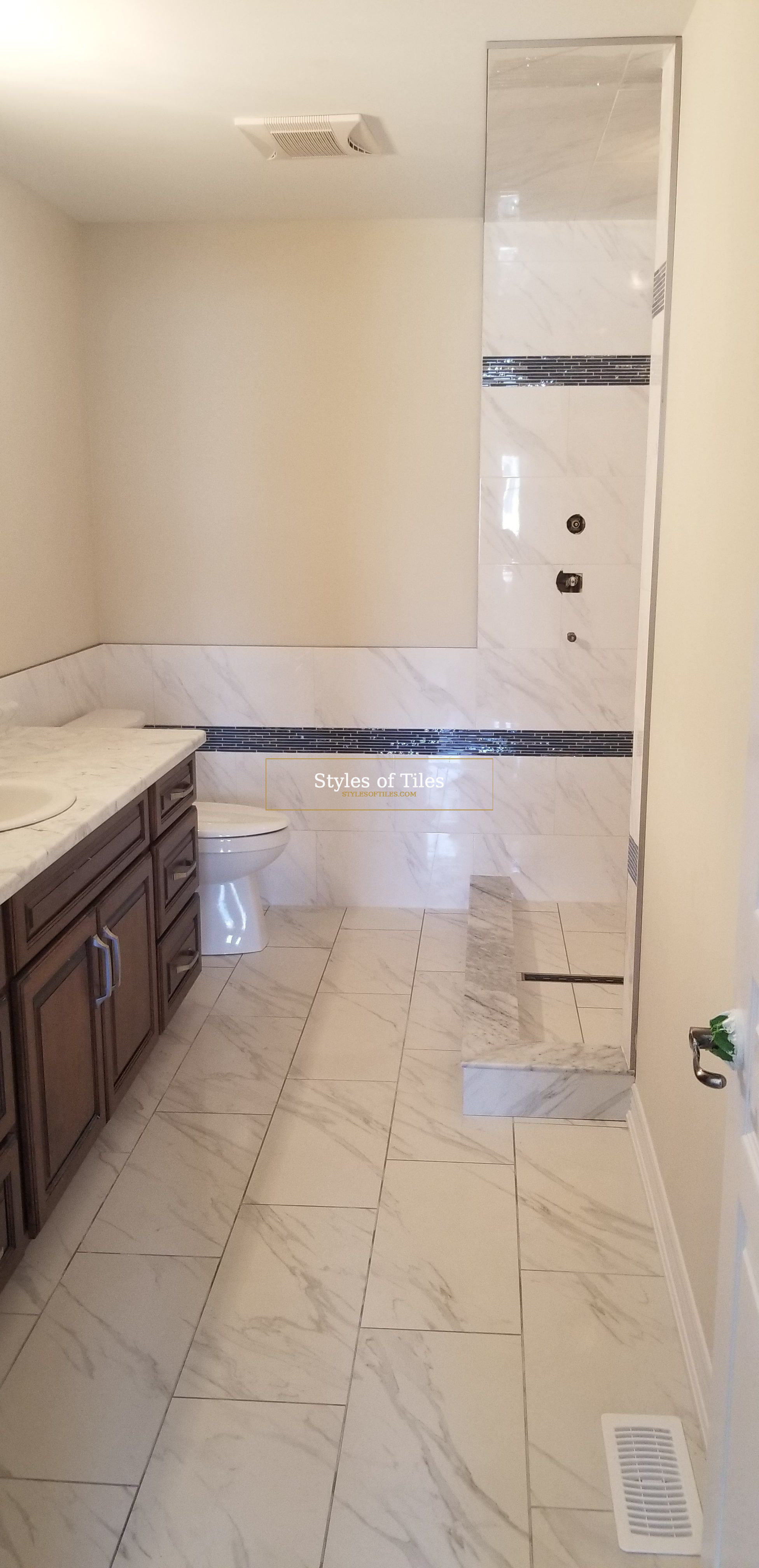 Finished bathroom with white marble-look rectangular floor tile running from the vanity to the shower