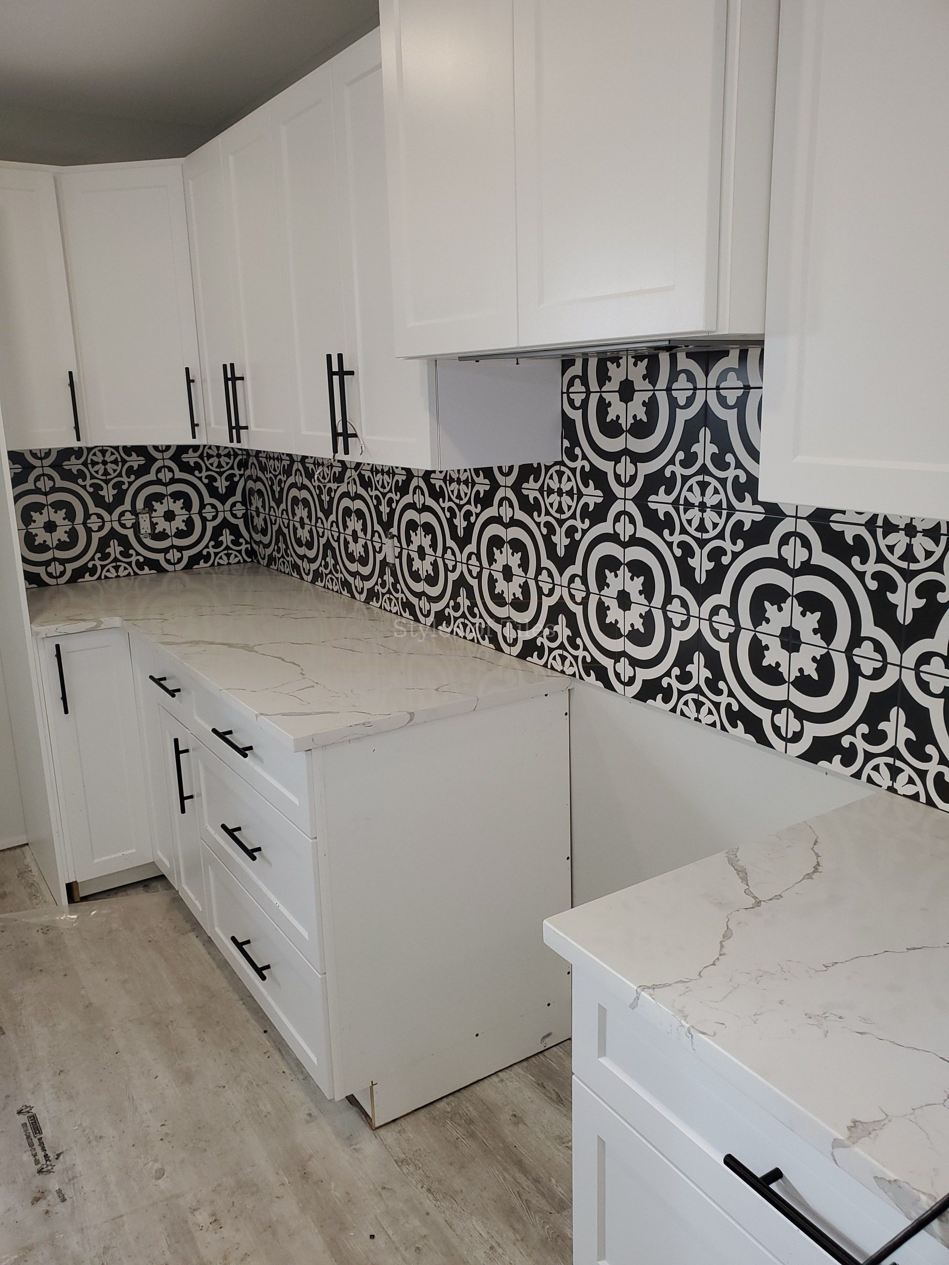 Black-and-white patterned tile backsplash under white cabinets in an L-shaped kitchen