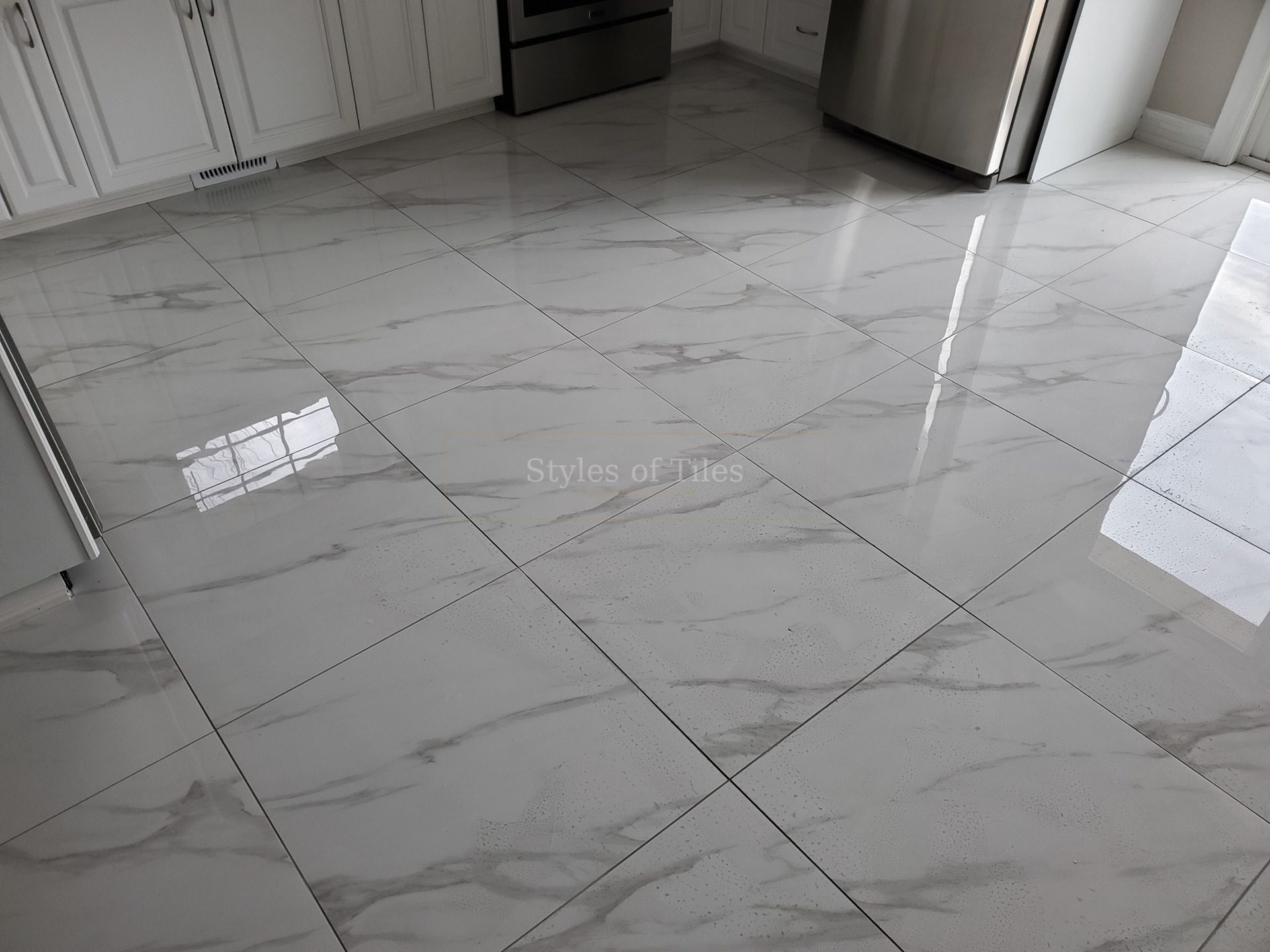 Polished marble-look large-format floor tile in a kitchen with white cabinets and stainless appliances