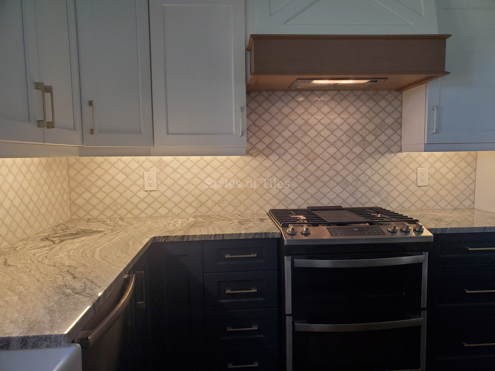 White arabesque tile backsplash behind a range, with a wood range hood and navy lower cabinets