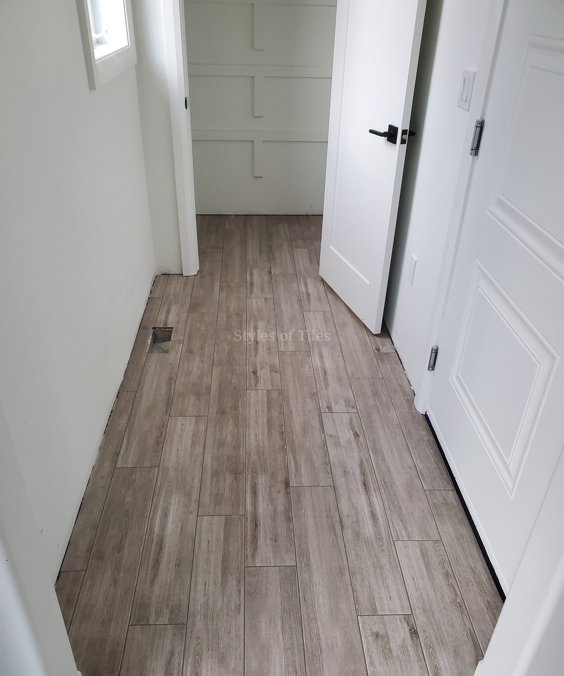 Grey wood-look plank floor tile running down a hallway past white doors