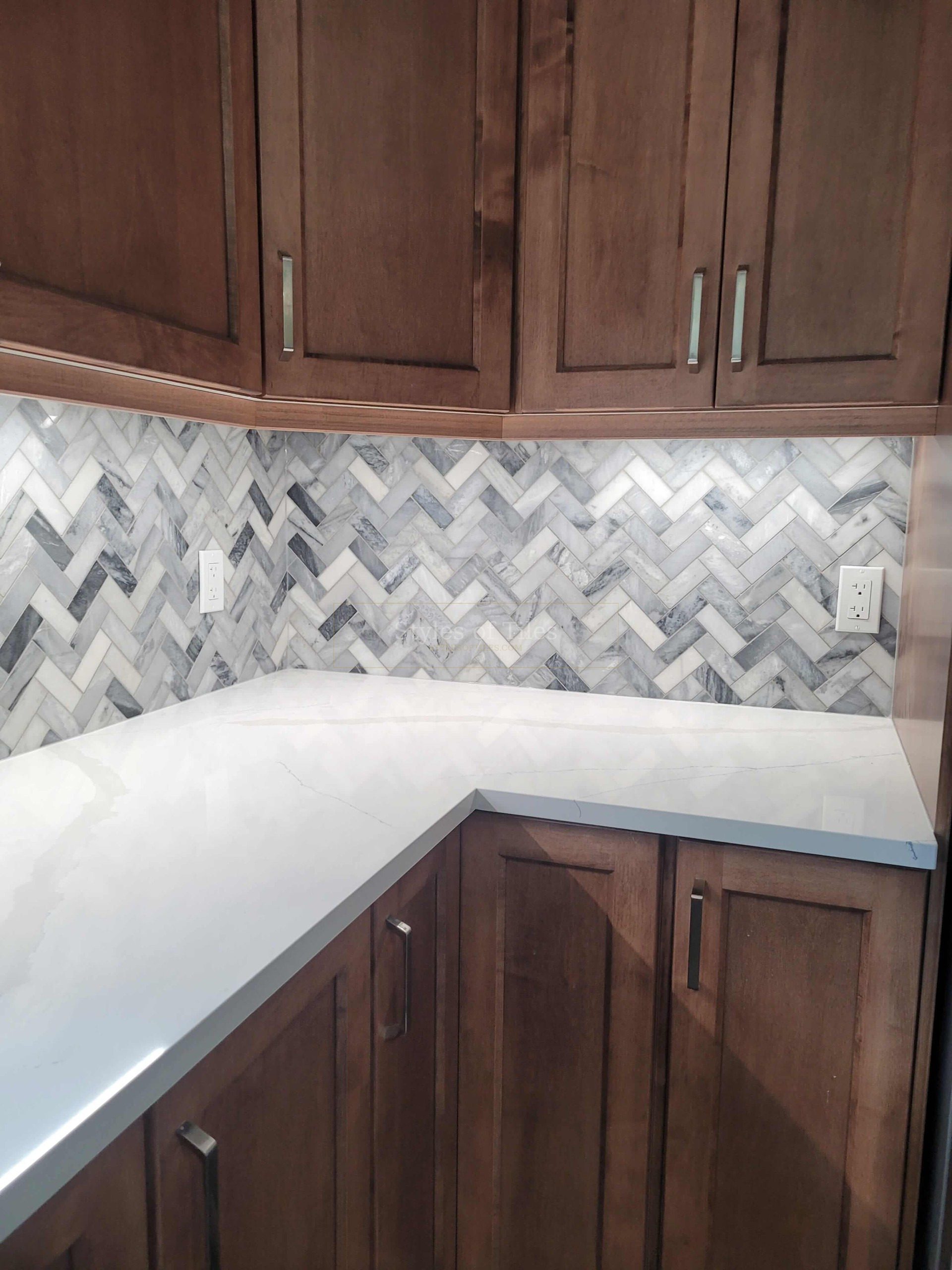 Grey-and-white marble herringbone mosaic backsplash in the corner of a kitchen with dark wood cabinets