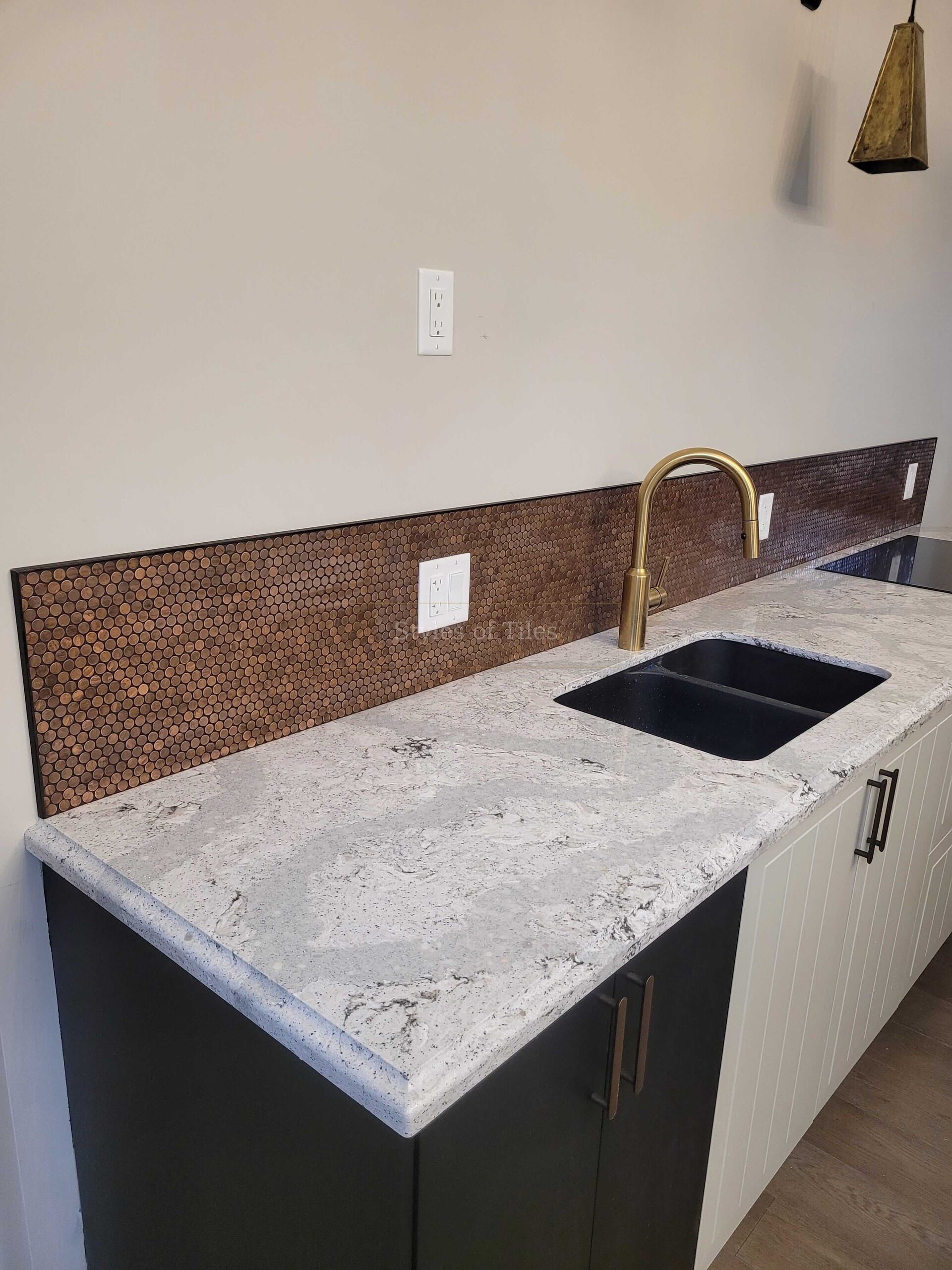 Copper penny-round tile backsplash behind a kitchen sink with a brass tap