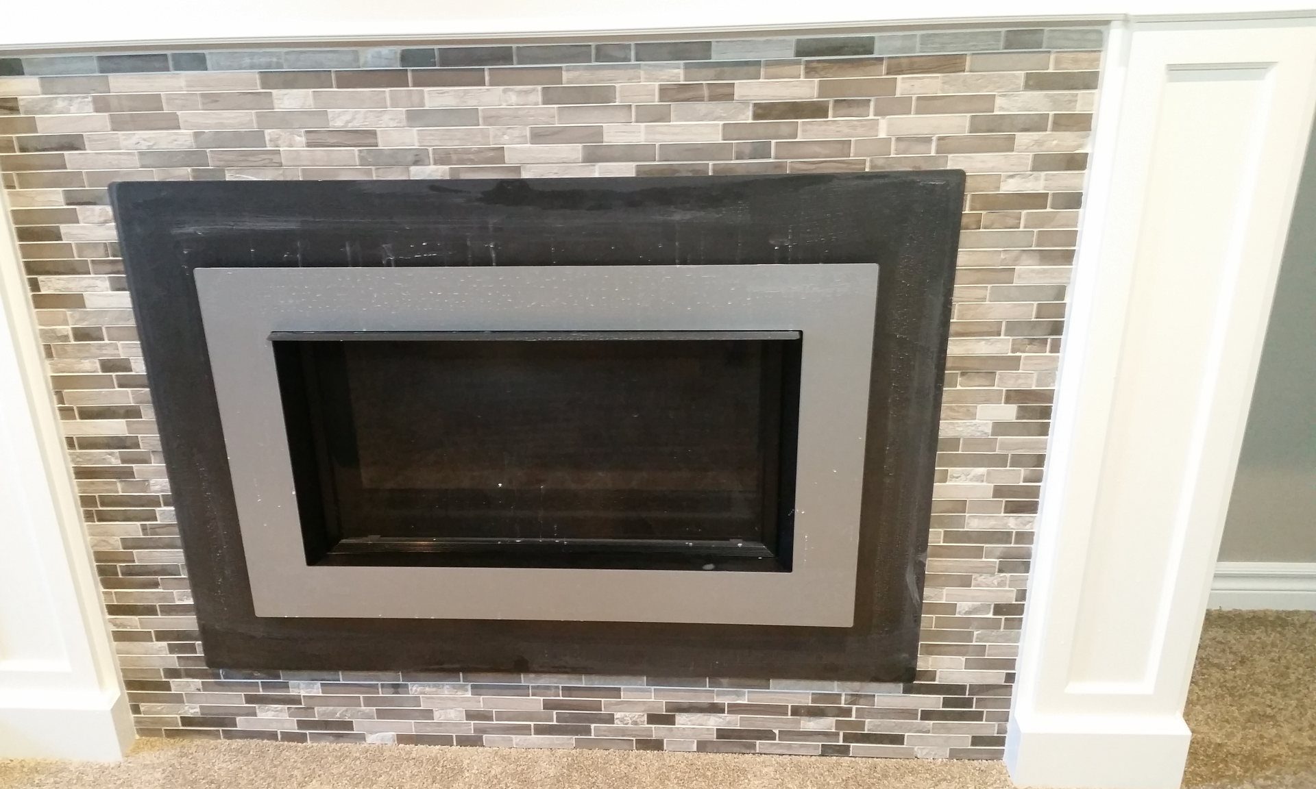 Glass and stone mosaic tile surround around a fireplace insert inside a white mantel