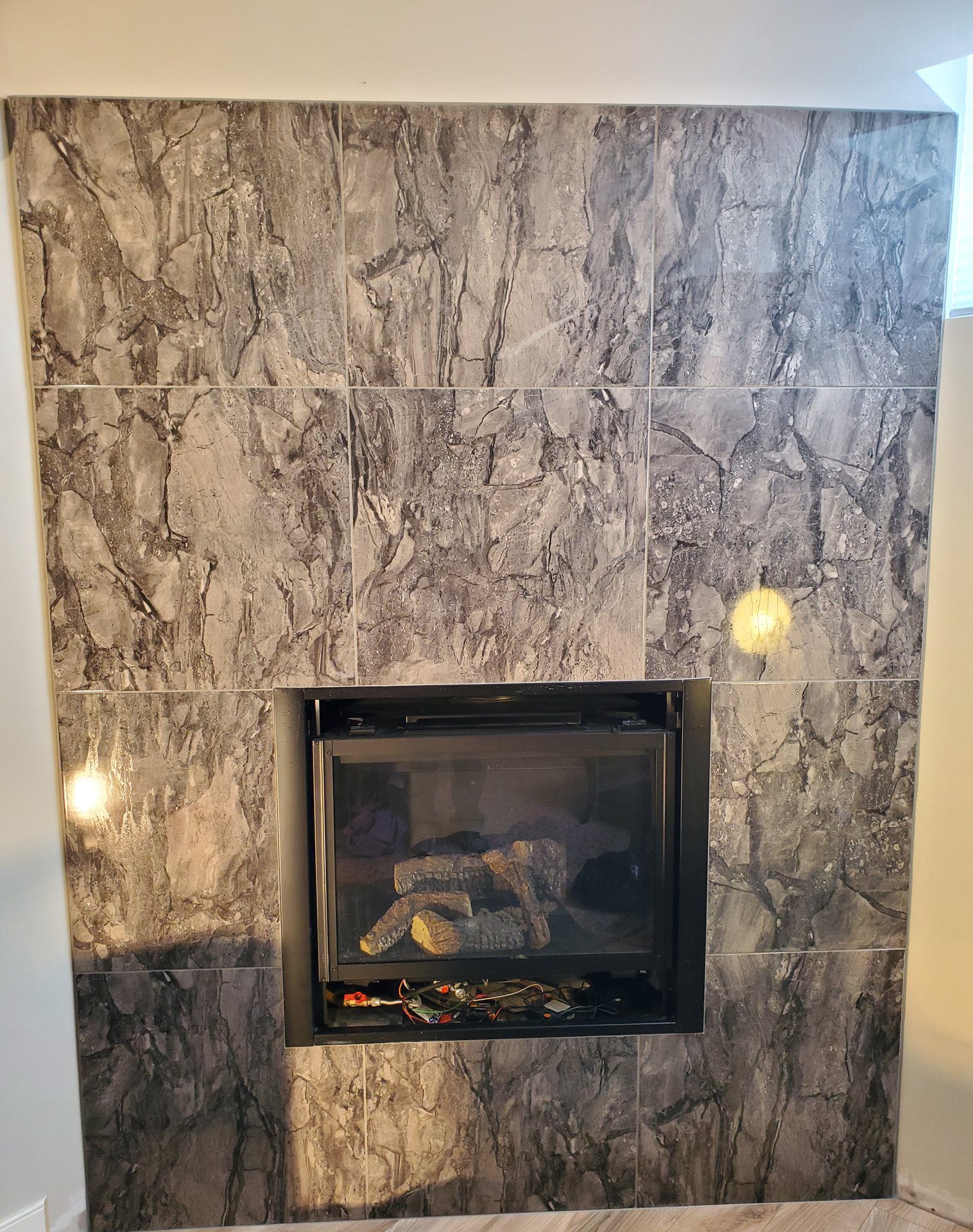 Fireplace wall in large-format grey marble-look porcelain tile cut tight around the firebox