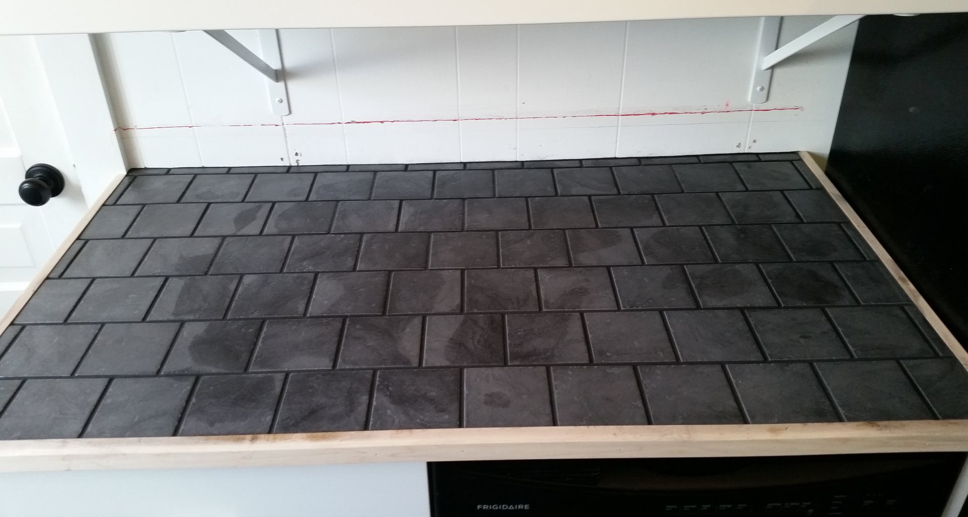 Countertop finished in dark slate-look tile laid in a brick pattern with a wood edge