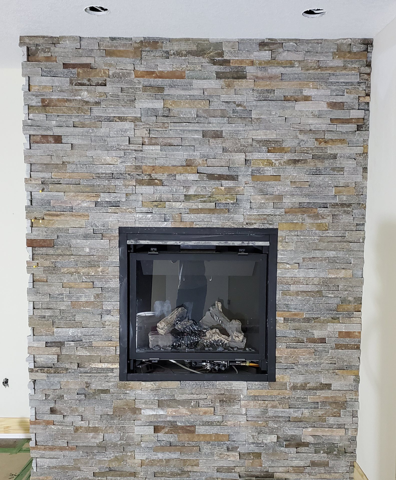 Gas fireplace in a floor-to-ceiling stacked stone surround in grey and rust tones