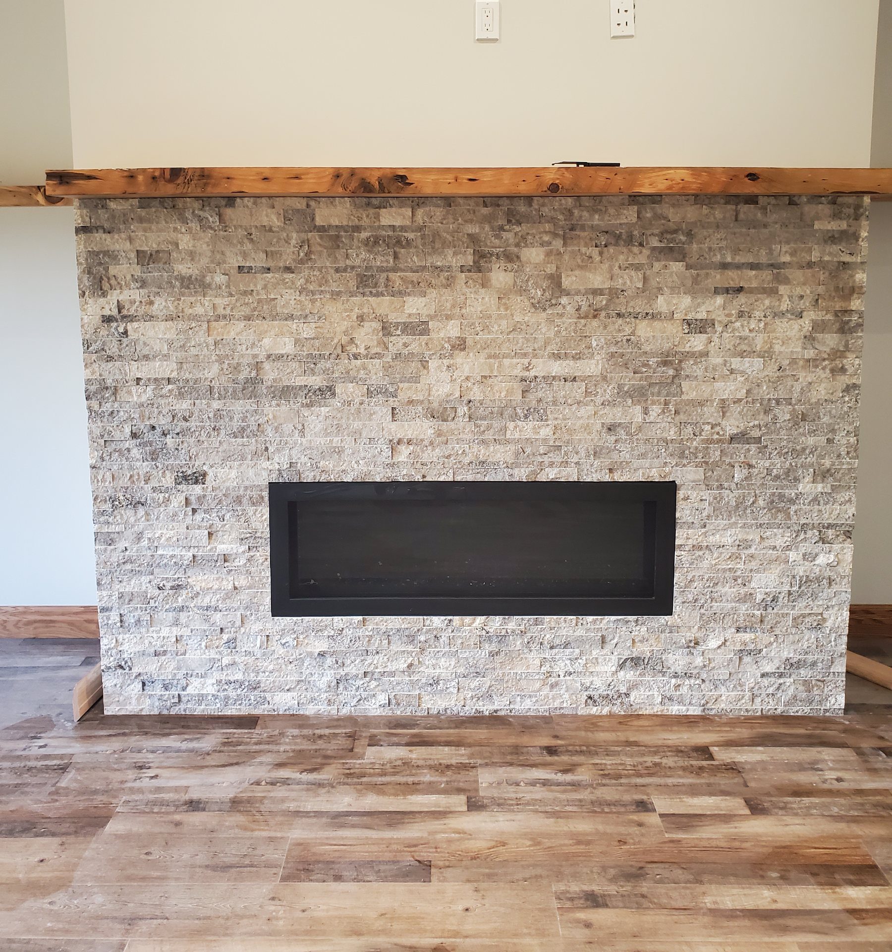 Linear fireplace in a split-face travertine surround under a rustic wood beam mantel