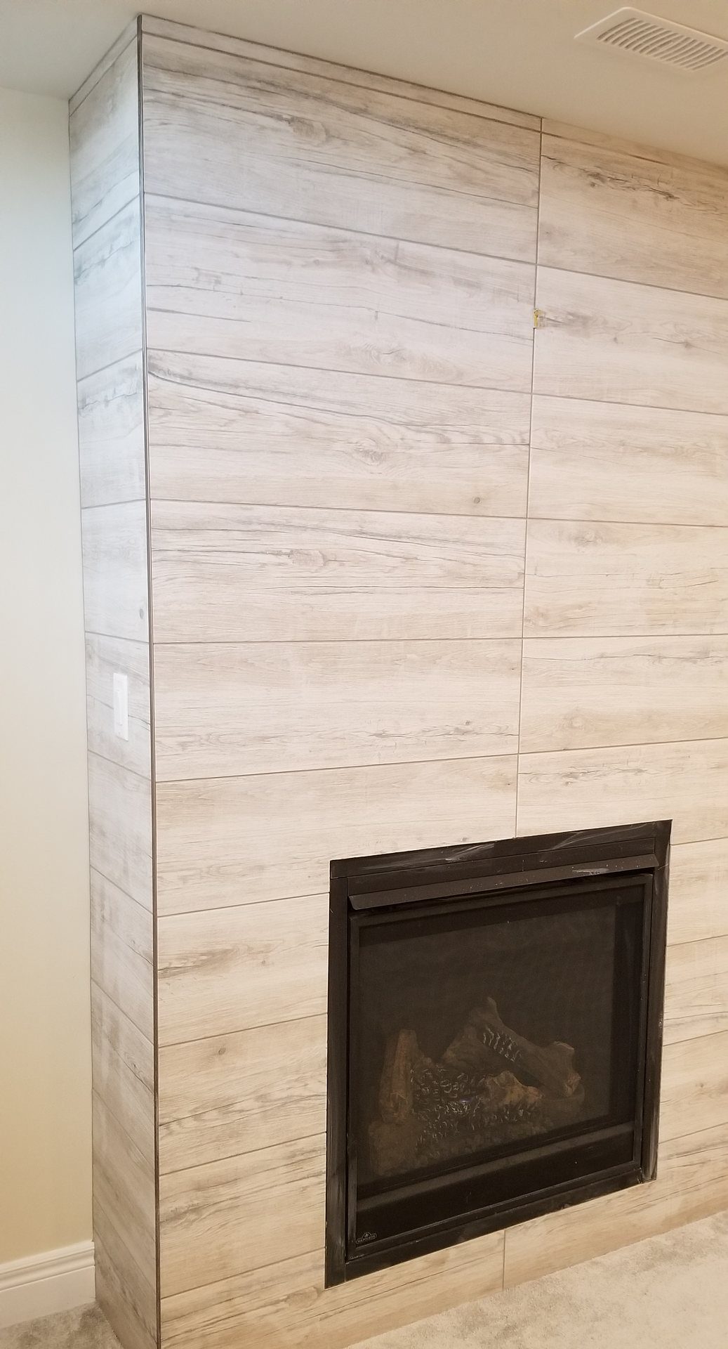 Floor-to-ceiling fireplace wall in light wood-look plank tile with the corner wrapped